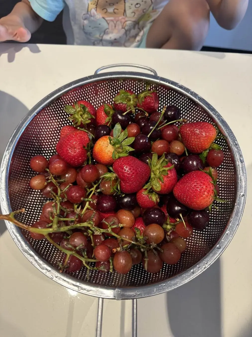 A colander of fresh strawberries, cherries and grapes, washed for a session